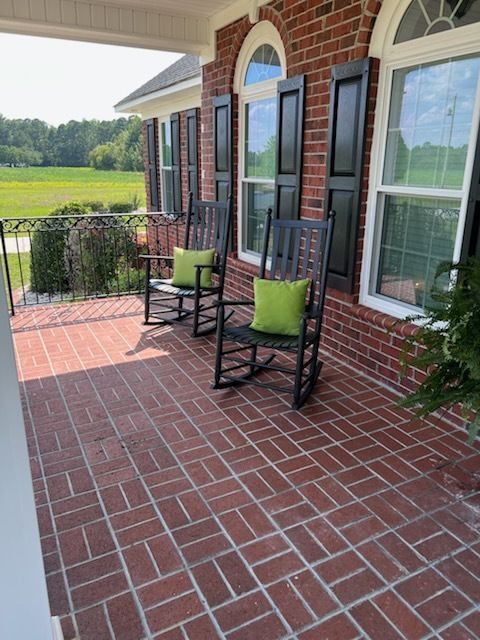 Brick porch with two black rocking chairs and green cushions beside a brick house and fields beyond