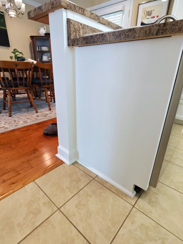 White folding safety gate blocking doorway between tiled kitchen and hardwood dining area