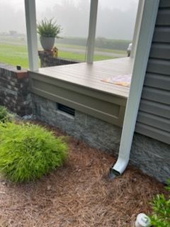Rain gutter downspout draining onto mulch beside a screened porch and deck in a foggy yard
