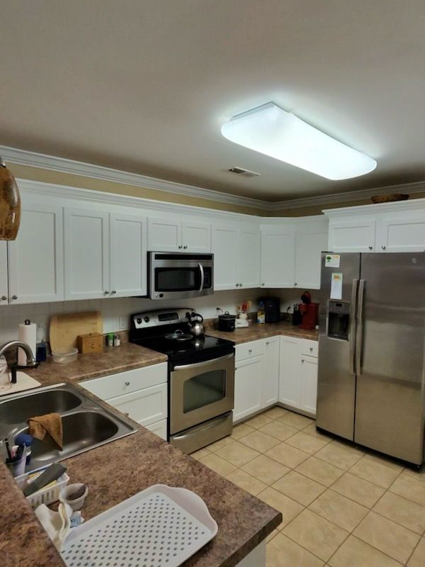 Modern kitchen with white cabinets, stainless steel appliances, and beige tile floor