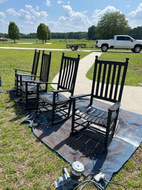 Three black rocking chairs on a blanket in a sunny grassy field with a white pickup truck nearby.