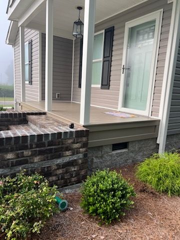 Front porch with a mint-green door, hanging lantern, brick steps, and small shrubs beside a house.