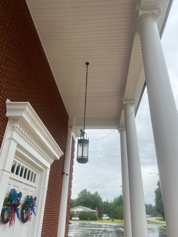 Covered porch with white columns, hanging lantern, wreath on door, and a rainy street beyond.