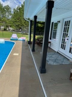 Backyard pool deck beside white house with black posts and glass doors