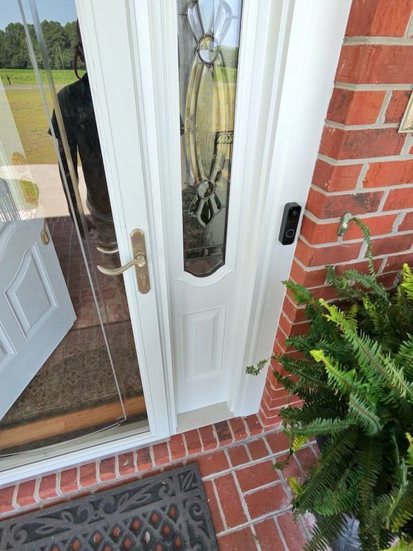 Front door with glass panels and brass handle beside brick wall, fern plants, and a welcome mat.