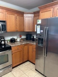 Small kitchen with wooden cabinets, stainless steel appliances, and light tile floor.