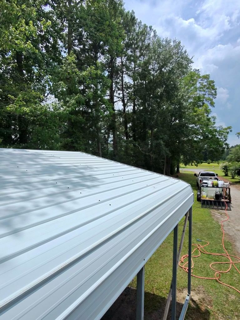 White metal roof beside trees; extension cord and work equipment on grass in the distance.