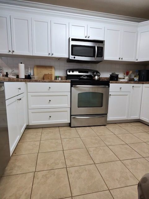Bright kitchen with white cabinets, stainless steel stove and microwave, and beige tiled floor.