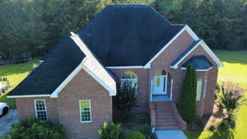 Brick suburban house with dark roof, front walkway, and landscaped yard in daylight