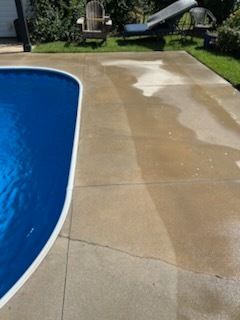 Wet concrete pool deck beside a blue swimming pool, with a darker dried patch near the top.