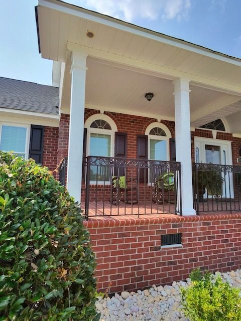 Brick front porch with white columns, red brick steps, black railing, and shrubs in front of a house