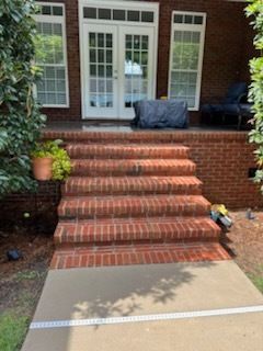 Brick front porch with central steps leading to white double doors and potted plants on either side
