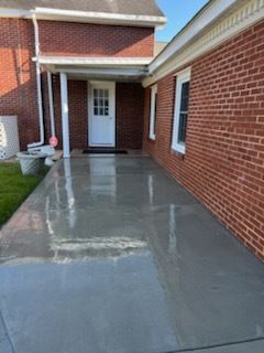 Covered brick walkway with a freshly finished gray concrete patio leading to a white front door.