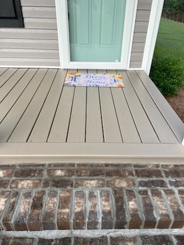 Front porch with a mint green door, gray deck boards, brick step, and a colorful doormat.