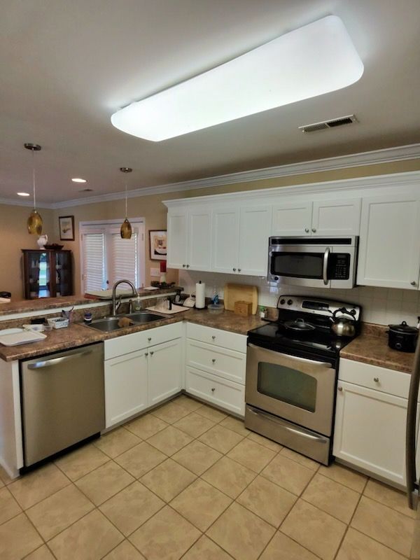 Modern kitchen with white cabinets, stainless appliances, tan tile floor, and central island under bright ceiling light