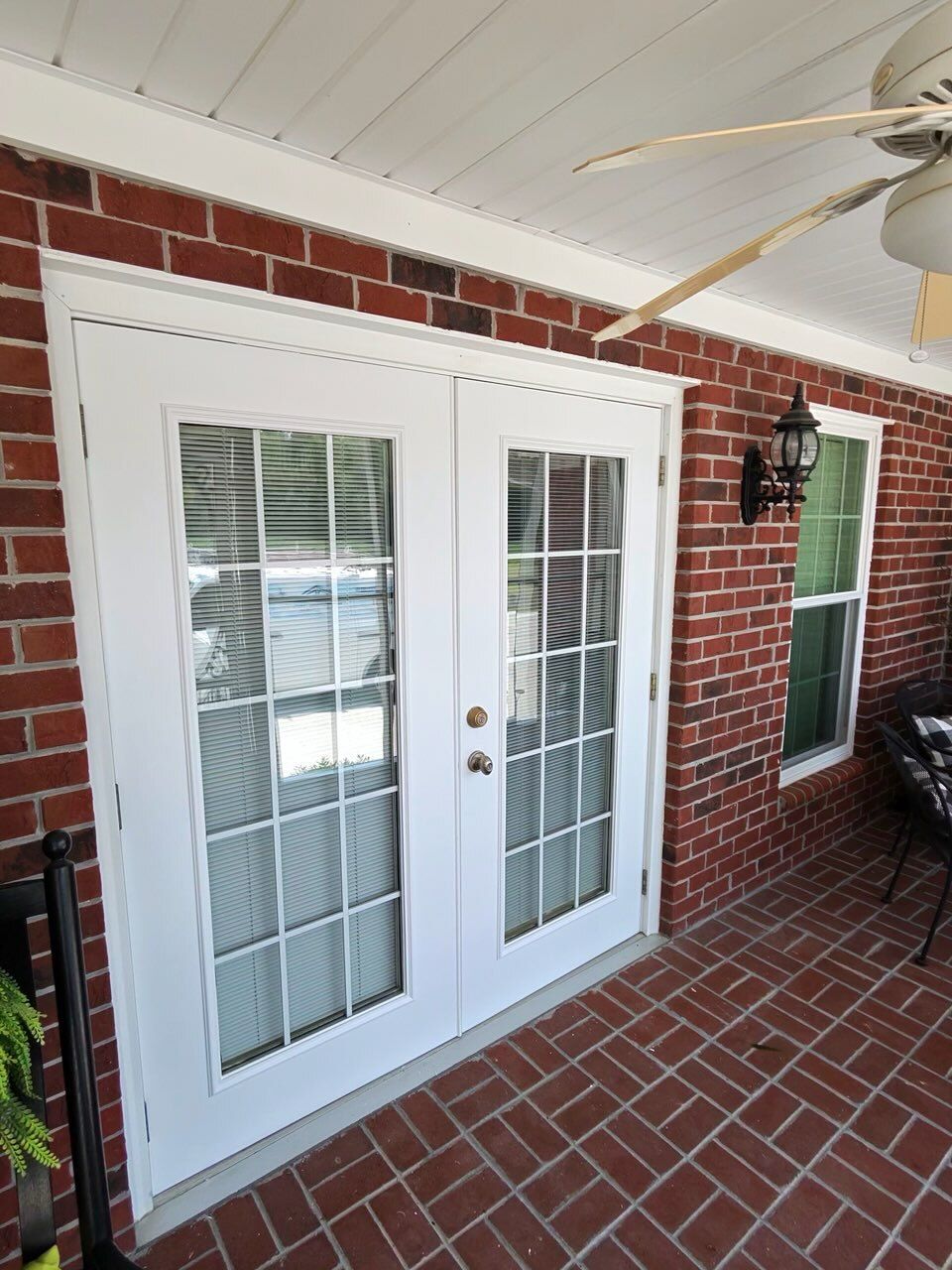 White French doors with glass panes on a brick patio, beside a wall-mounted lantern and window.