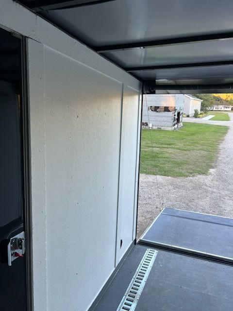 Interior view of an open trailer ramp with white walls and a glimpse of grass and a road outside