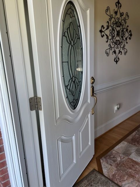 White front door with oval glass panel in a bright hallway with hardwood floors and wall decor