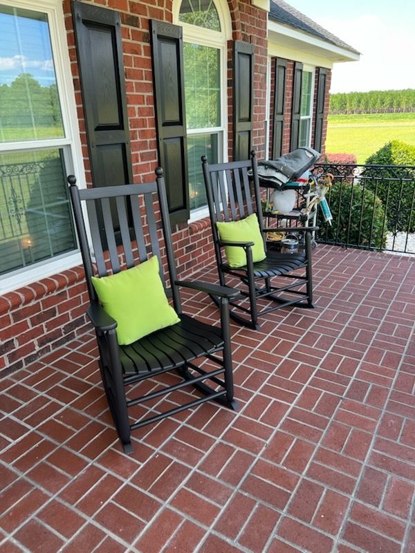 Two black rocking chairs with green cushions on a brick porch beside a house