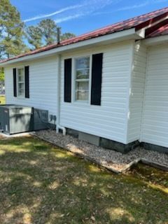 White-sided house exterior with black shutters, red roof, and HVAC unit beside a grassy yard.