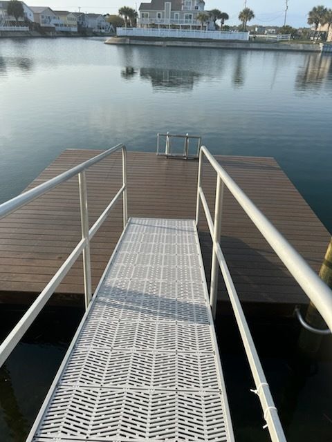 Narrow dock ramp with white railings leading to a floating platform on calm water