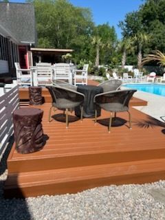 Wooden deck with patio chairs and table beside a backyard swimming pool on a sunny day