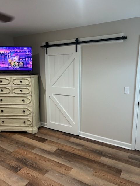 Bedroom with white barn door on black rail, wood floor, and dresser with TV against beige wall.