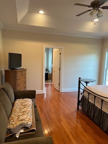 Bedroom with bed, sofa, dresser, ceiling fan, and open doorway to a hallway.