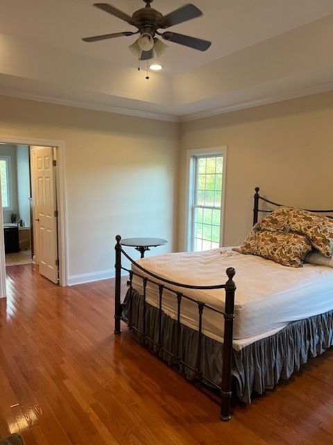 Empty bedroom with hardwood floors, black metal bed, beige walls, ceiling fan, and open doorway to a hall