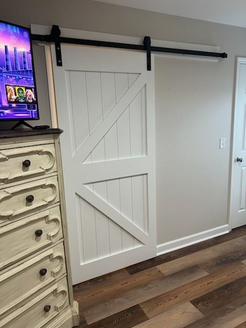 White barn-door style sliding closet door with black rail in a room, beside a dresser and wood floor