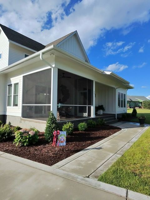 Single-story house with screened front porch, white siding, and landscaped yard under a blue sky
