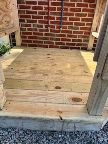 Wooden porch deck with a brick wall and vertical posts, viewed from the front.