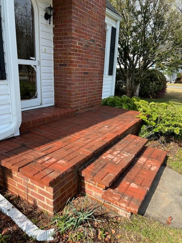 Brick front porch with three damaged steps beside a white door and brick wall