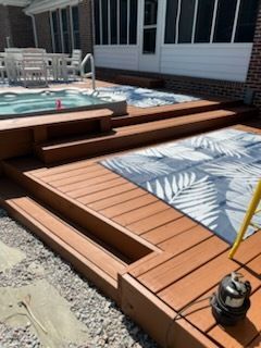 Wooden pool deck with steps, built-in planter, and patterned outdoor rug beside a swimming pool