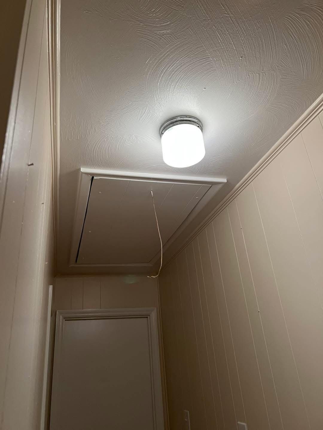 A narrow hallway with a closed attic access panel on the ceiling, light fixture above.