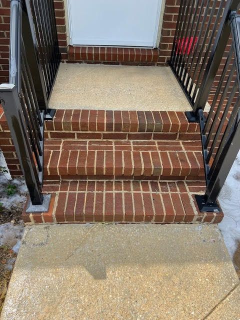 Brick steps leading up to a door with black handrails on a concrete landing.