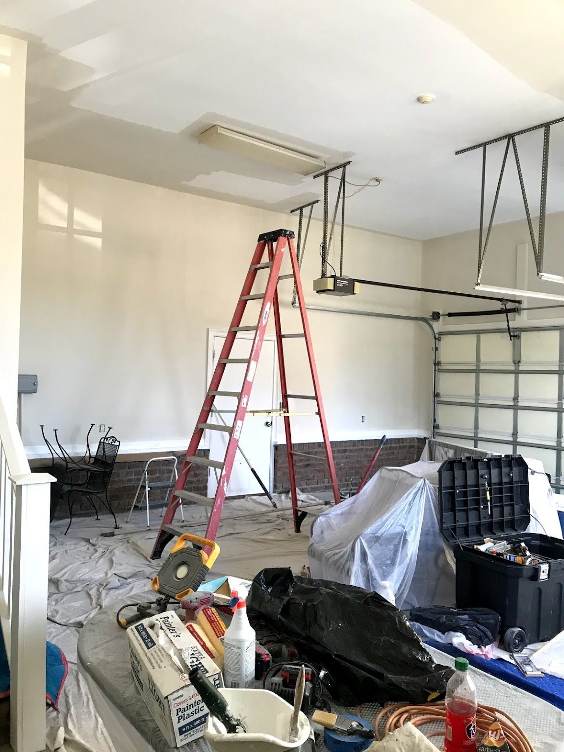 Garage interior under renovation; red ladder, tools, covered items, and exposed wiring.