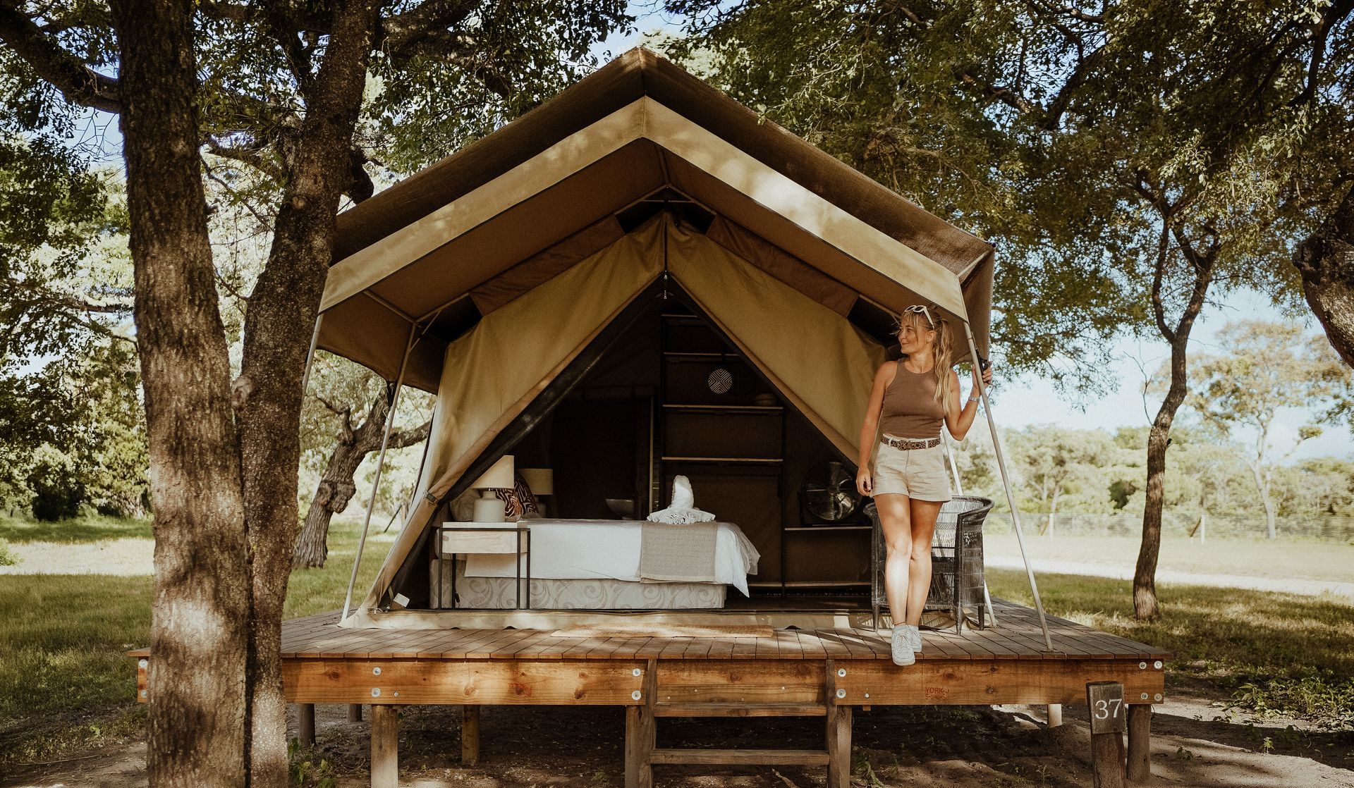Open-air safari tent cabin with a woman standing on the porch in a wooded campsite