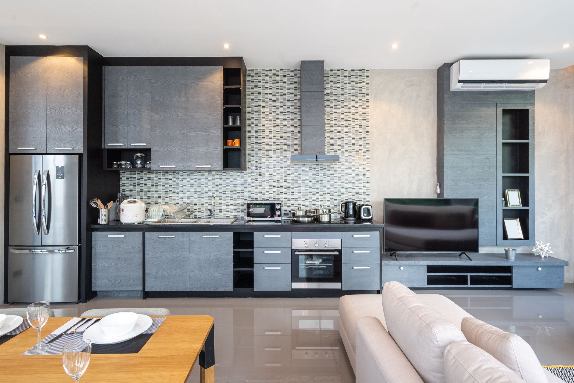 A modern, open-concept kitchen and living area featuring grey cabinetry, stainless appliances, and a mounted TV.