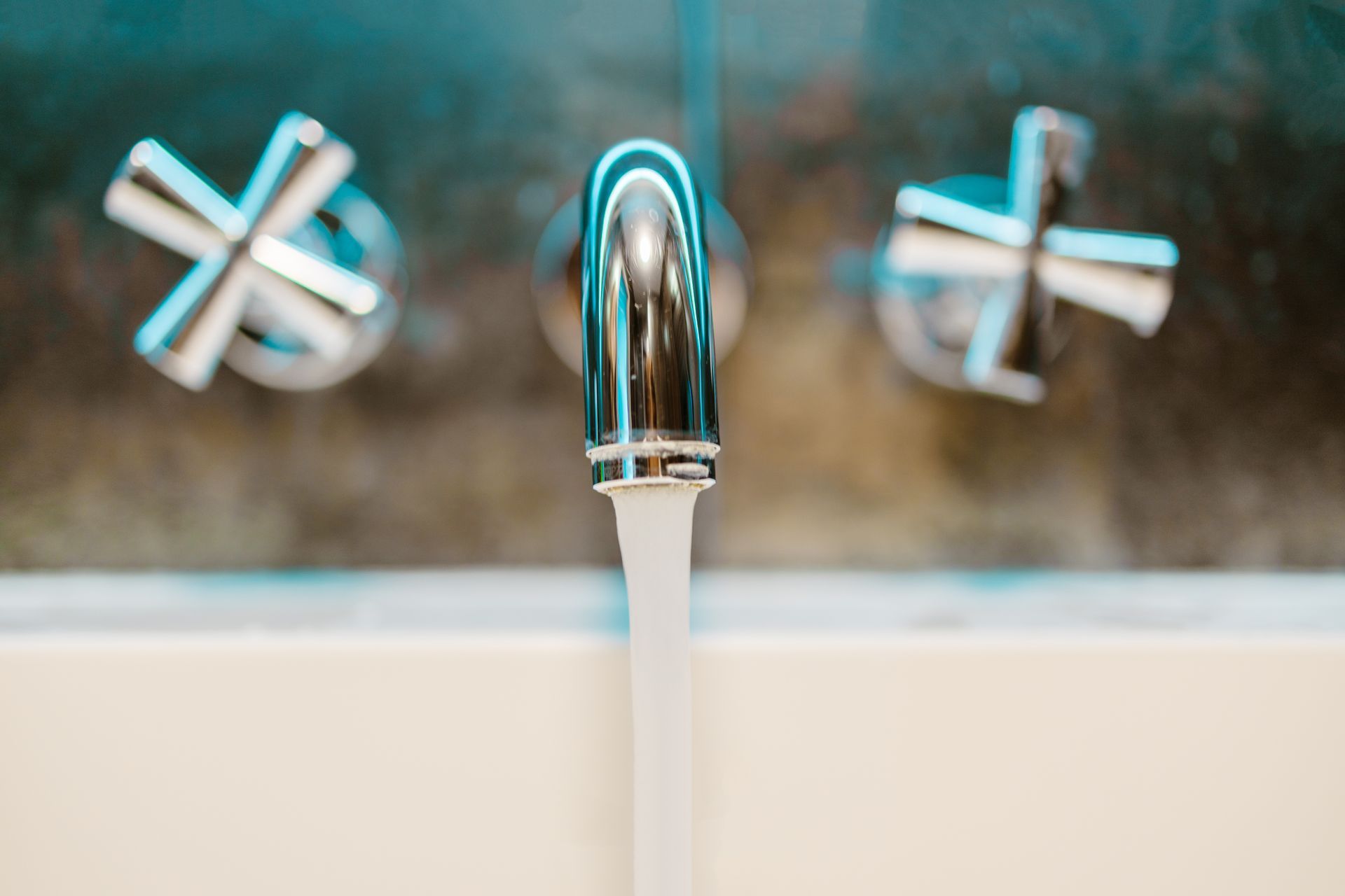 Chrome bathroom faucet with cross handles, running a steady stream of water into a white sink.