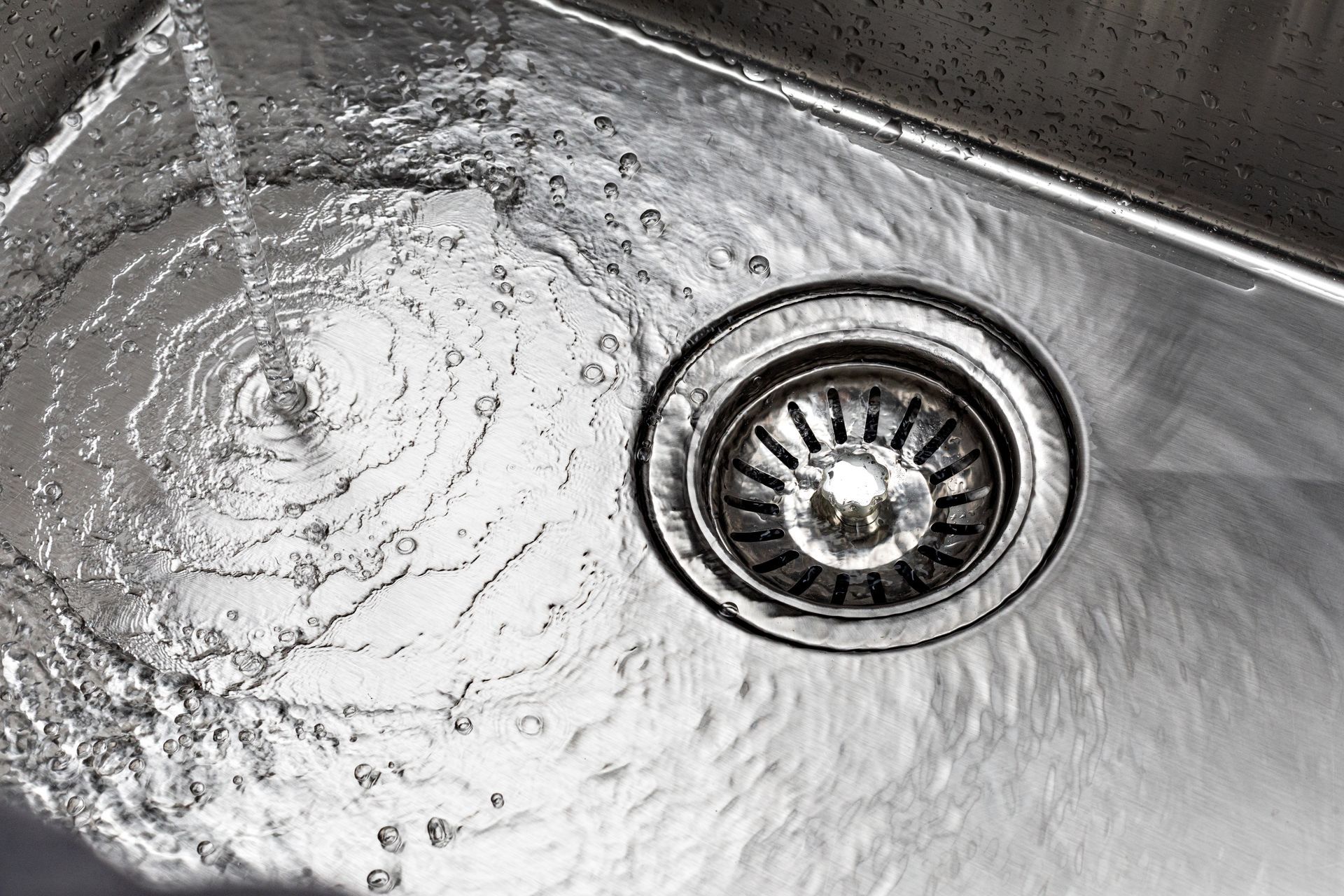 Water flows from a faucet into a stainless steel kitchen sink toward the drain.