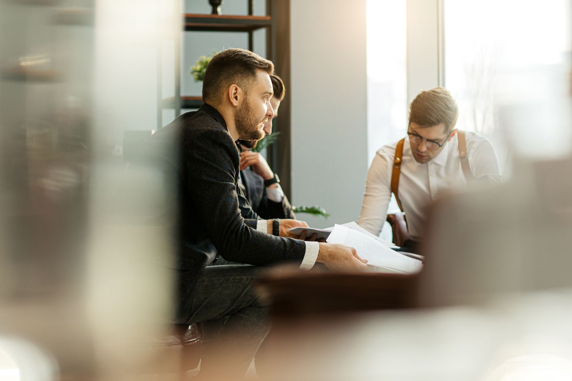 Professionals in business attire review documents and hold a collaborative meeting in a bright, modern office space.
