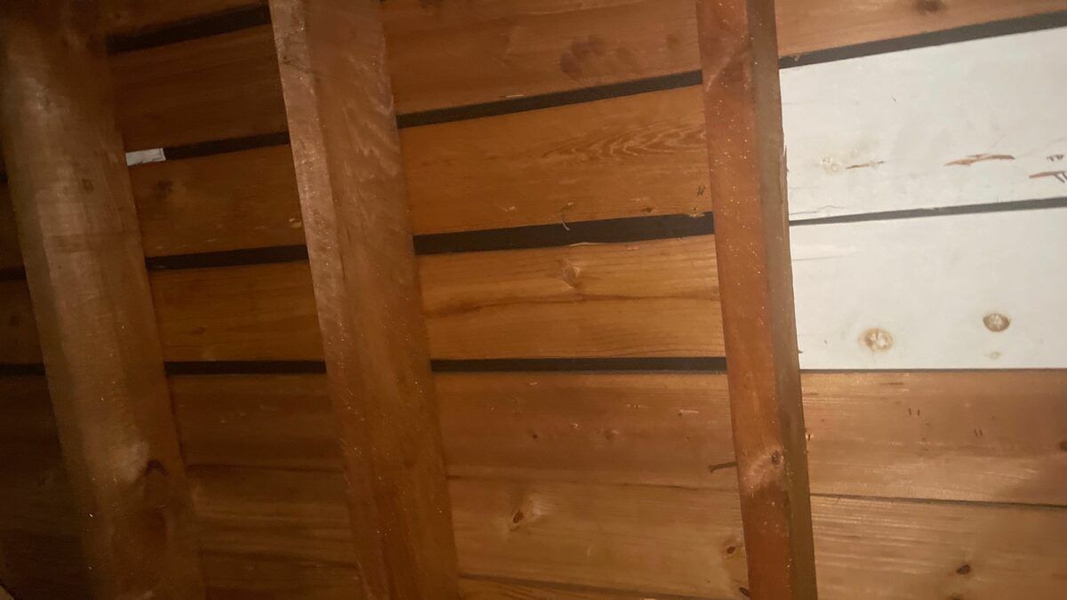 Wooden attic wall with exposed beams and a small white panel on the right