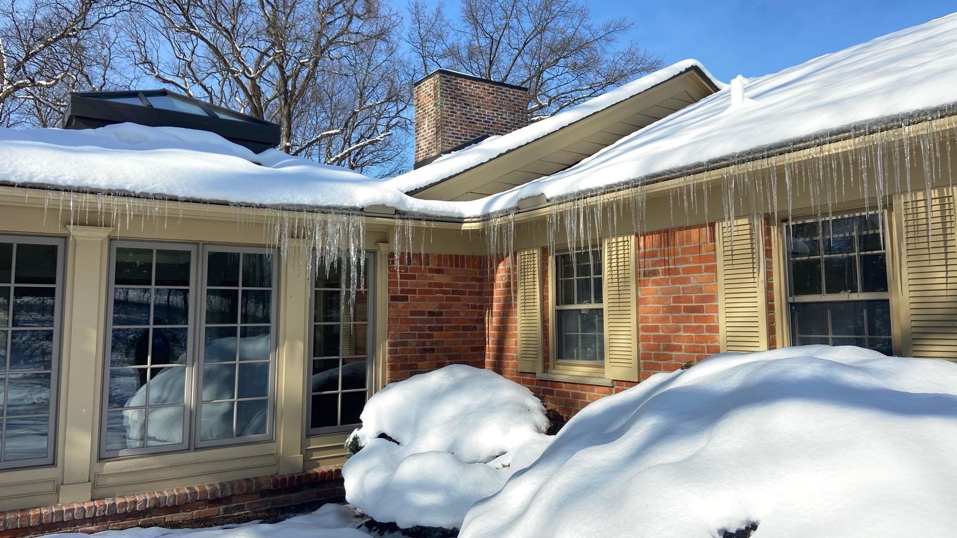 Snow-covered brick house with icicles hanging from the roof on a bright winter day