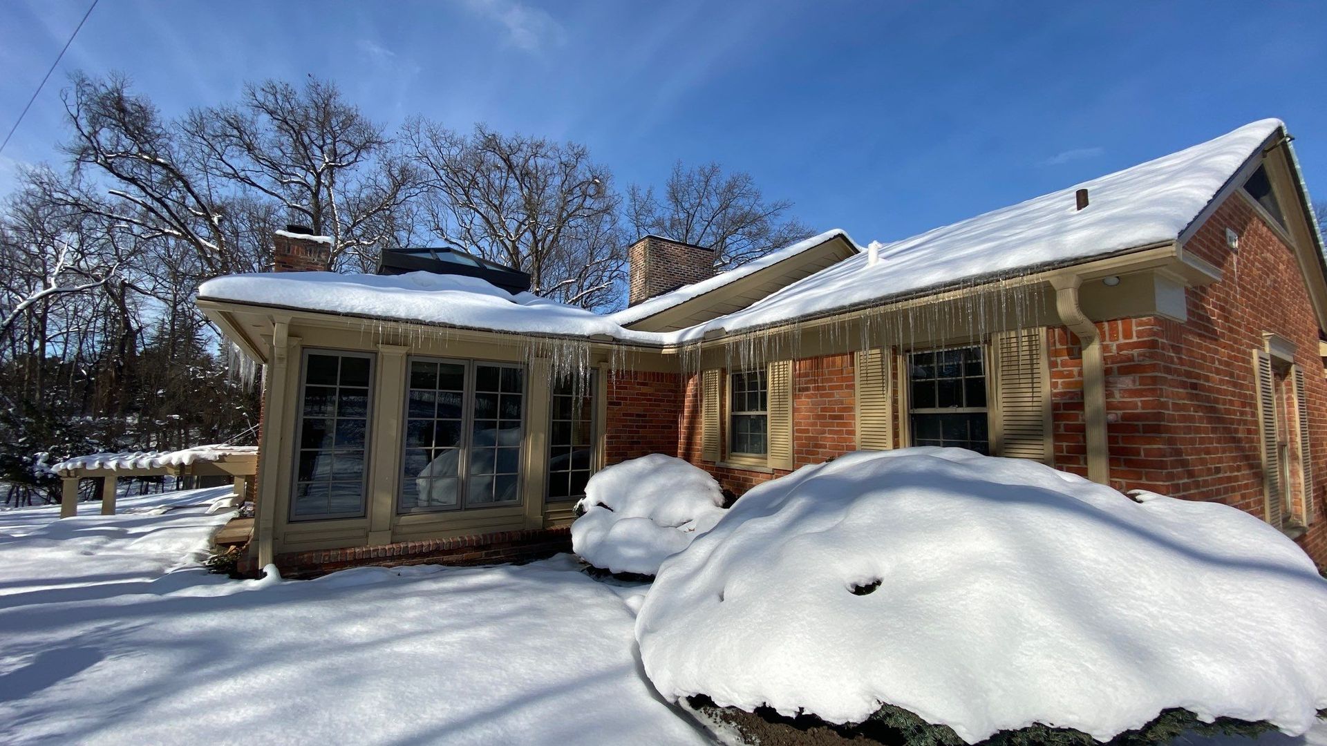 Snow-covered brick house with a screened porch on a bright winter day