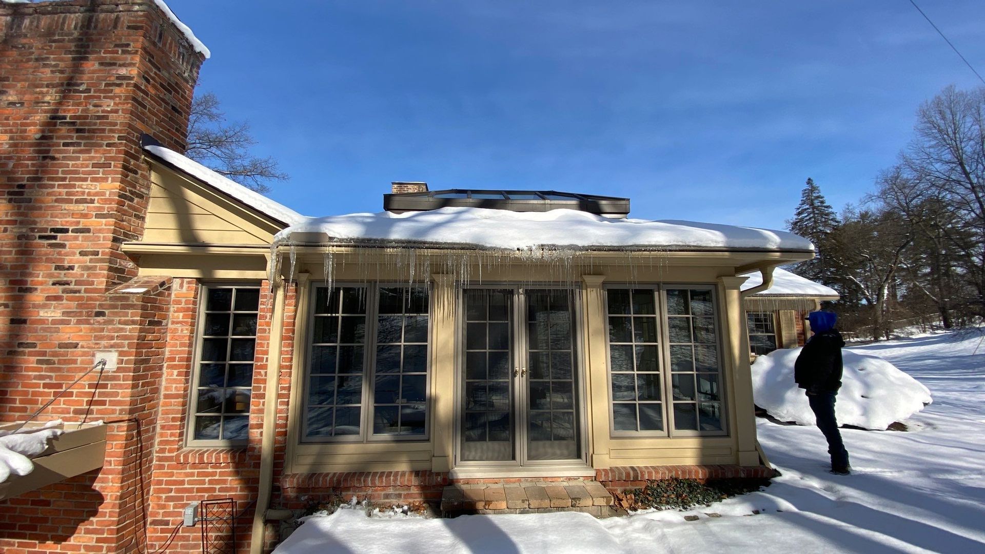 Snow-covered house with large windows and a person standing outside on a sunny winter day