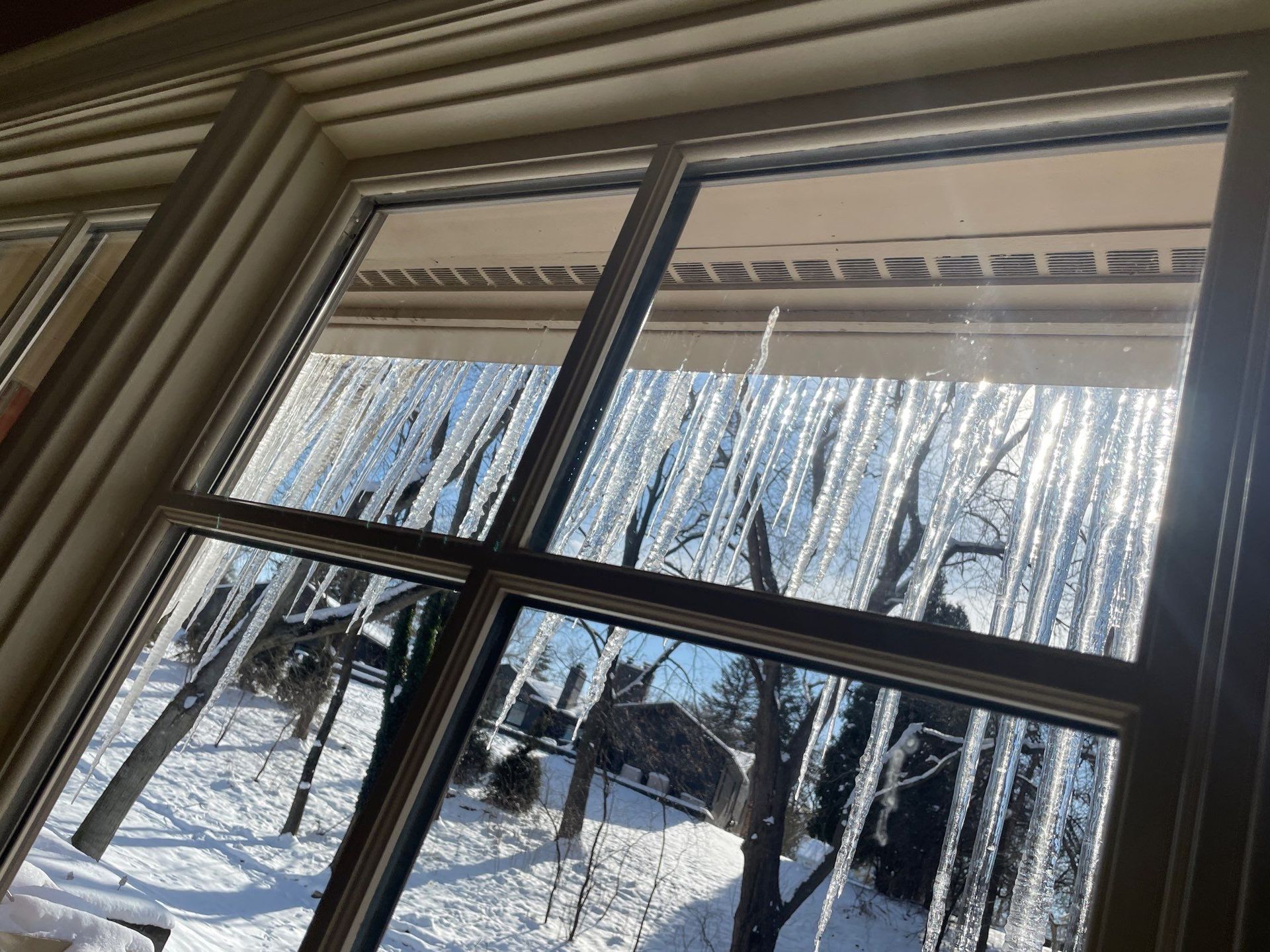 Snowy backyard seen through a window with icicles hanging from the roof edge