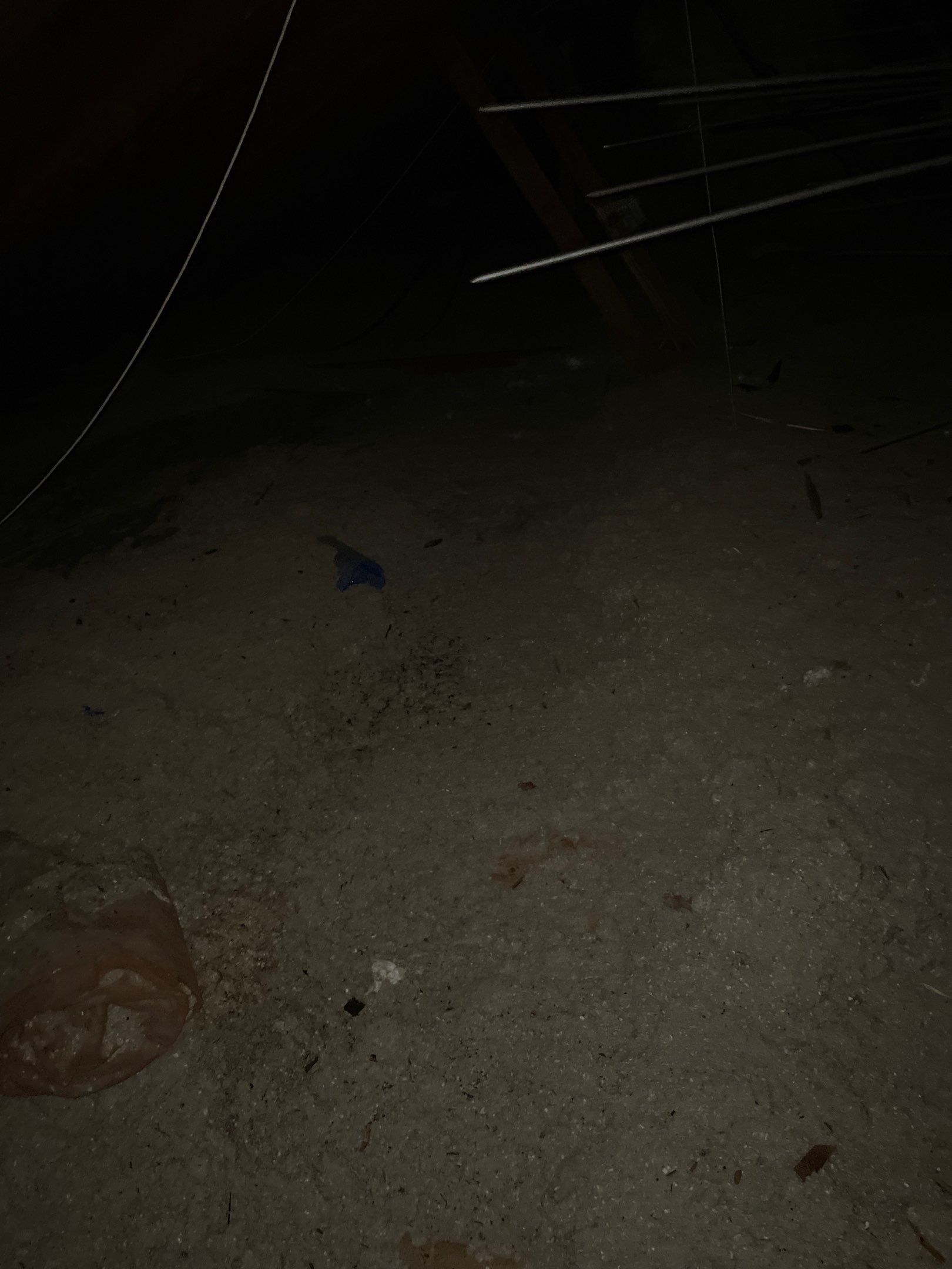 Dimly lit sandy ground at night with a few scattered small objects and a partial circular object in the corner