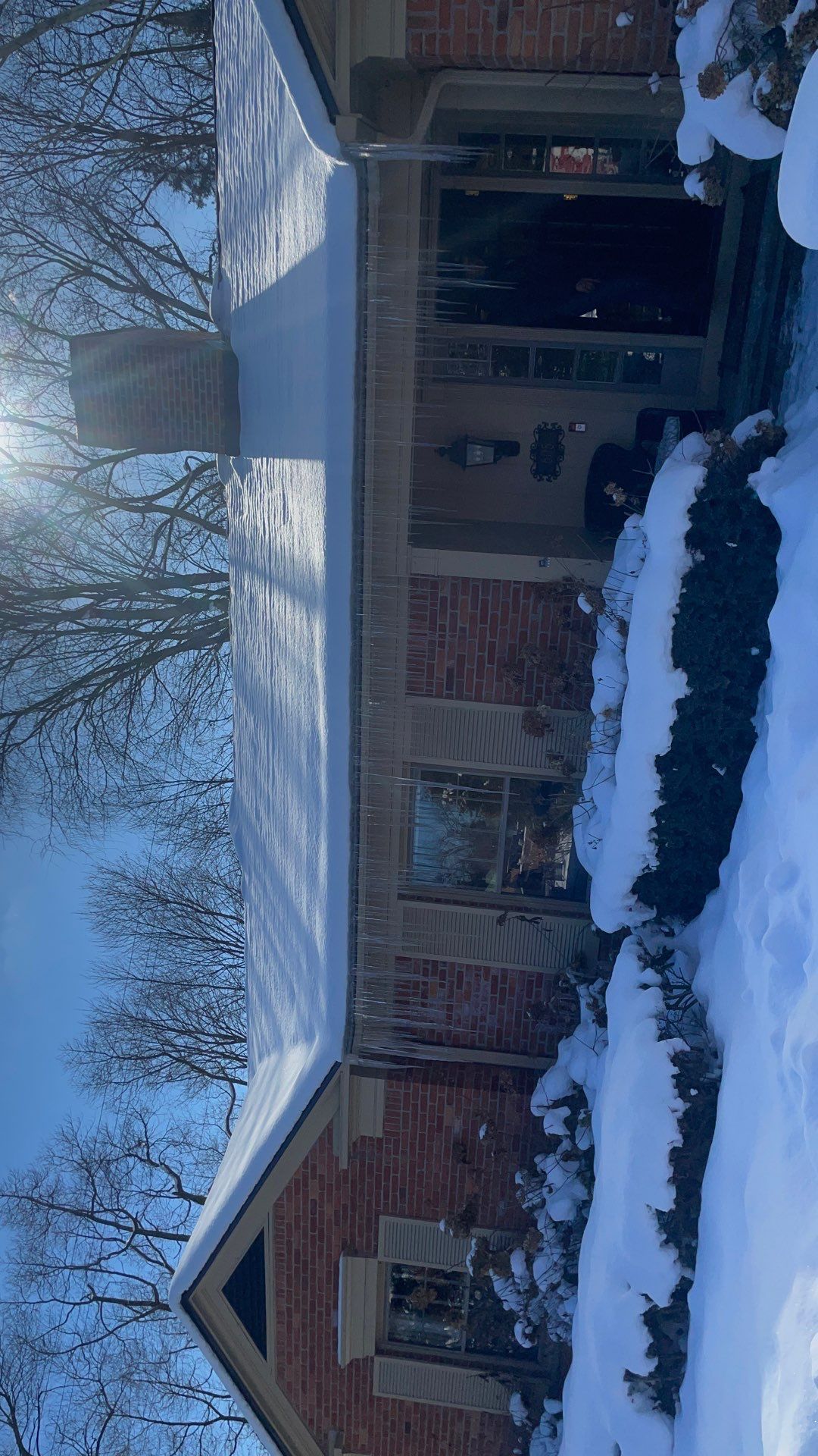 Snow-covered brick house with a front porch and trees in winter