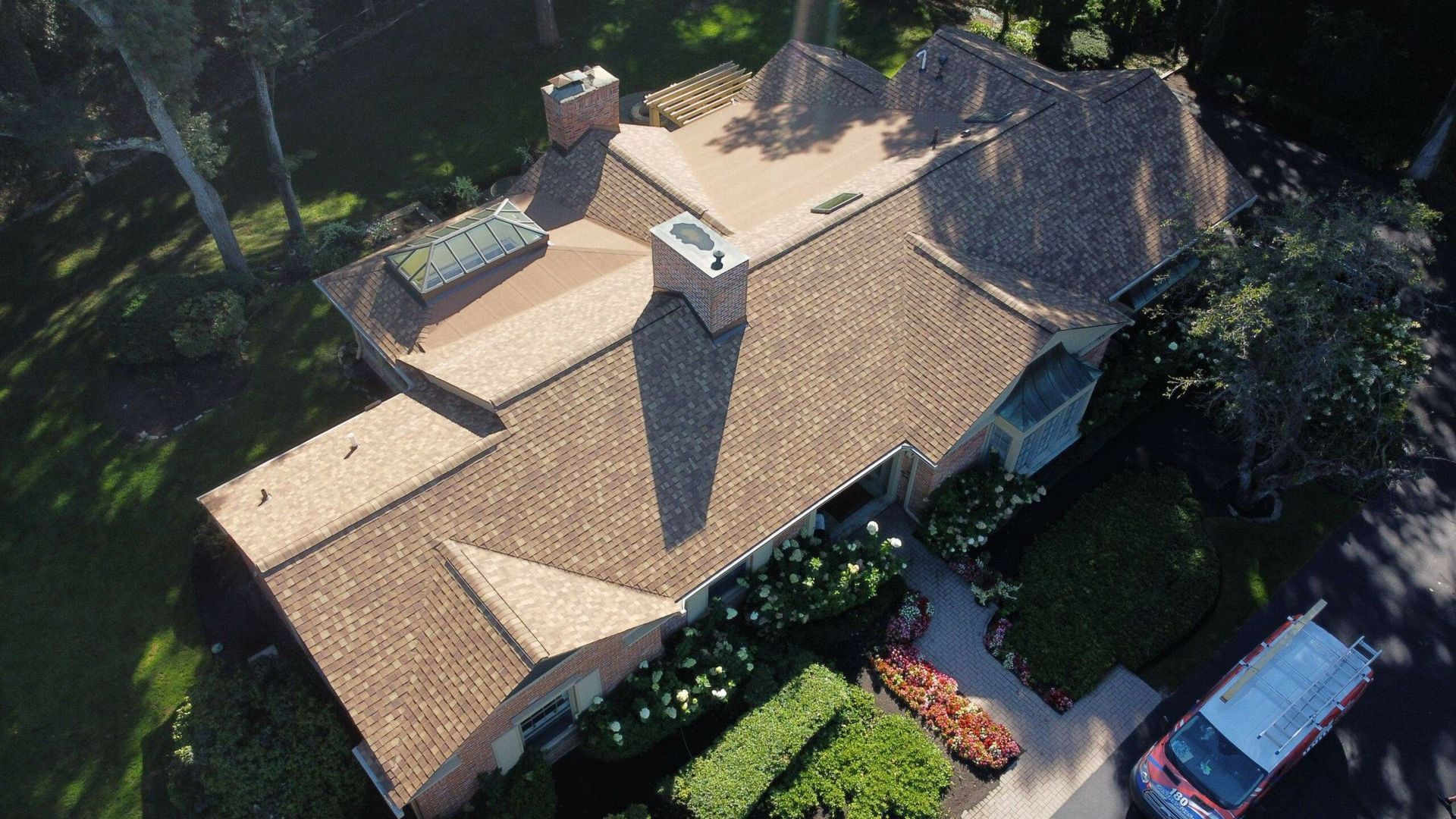 Aerial view of a tan-roofed house with trees and a driveway with a red car.